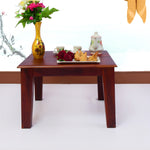 A wooden square coffee table in a living room setup with a vase of flowers and a cup of tea on top.