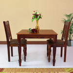 A solid wood dining table with a rectangular shape and two matching chairs, all in a maple finish, arranged in a living room setting with a floral vase on the table.