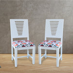A pair of white wooden dining chairs with a floral fabric seat cushion.