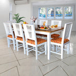 White finish wooden 8 seater dining table set with chairs having red and orange cushions, set in a bright room with tile flooring.