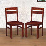 Two wooden dining chairs with a honey finish, displayed against a white background with a textured wall.