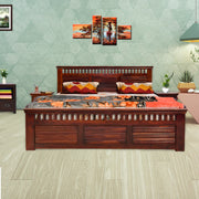 A wooden king-size bed with storage drawers in a honey finish, positioned in a bedroom setting with decorative pillows and a wall painting in the background.