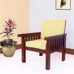 A solid wood single seater sofa with maple finish and beige fabric cushioning, placed in a room with a potted plant to the side.