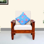 A single seater wooden sofa with a maple finish, featuring a white cushion with a blue floral pillow on it, placed in a room with light walls.