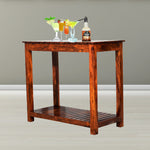 A small rectangular solid wood table with a teak finish, featuring a lower shelf, displayed in an interior setting with a couple of glasses and bottles on top.