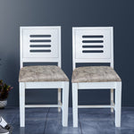 A pair of white finished mango wood dining chairs with upholstered seats, pictured against a neutral background.