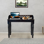 Black desk with a laptop, books, and a plant in a room with a gray wall and a small table.