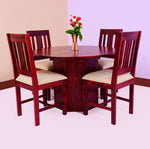 A round dining table with four chairs made of sheesham wood, featuring beige fabric cushions on the chairs. A vase with flowers is placed on the table.