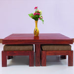 A rectangular solid wood coffee table with stool in brown color, placed on a white floor against a purple background, with a yellow vase on top of the table containing flowers.