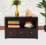 A brown wooden chest of drawers with three drawers, placed against a wall with a decorative vase on top and some books and a teddy bear arranged on the drawers.