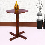 A wooden round center coffee table in a honey teak finish, with a decorative vase on top, placed against a wall with two decorative wall-mounted vases.