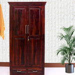 A brown sheesham wood wardrobe with two door and two drawer units, with a potted plant to the side.