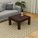 A solid wood coffee table in Kapasi brown finish placed on a zigzag pattern rug, with a grey sofa and a decorative item on the table.