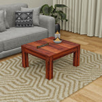 A solid wood coffee table in Kapasi brown finish placed on a zigzag pattern rug, with a grey sofa and a decorative item on the table.