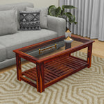 A solid wood coffee table with a glass top and a lower shelf, placed on a patterned rug. The table is brown in color and has a modern style.