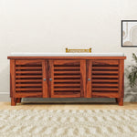 A wooden shoe rack with cushion seat placed on a plush carpet, featuring three brown wooden doors and a top shelf for storage.