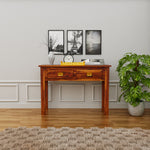 Wooden desk in a room with framed pictures on the wall and a plant.