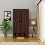 Wooden wardrobe in a room with a plant, lamp, and framed picture on the wall.