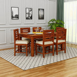 Wooden dining table set with chairs in a room with framed pictures on the wall.