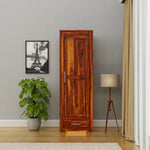 Wooden wardrobe in a room with a plant, lamp, and framed picture on the wall.