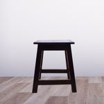 Wooden stool on a wooden floor with a white wall background