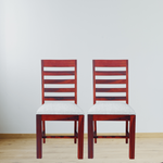 Two wooden chairs with white cushions on a light wooden floor and white wall background