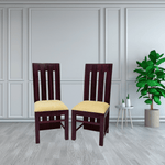 Two wooden chairs with yellow cushions in a room with a plant and small table.