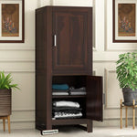 A wooden wardrobe in walnut finish with an open door showing neatly folded clothes inside, placed in a room with decorative wall paintings.