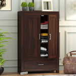 A wooden bookshelf with drawer storage in a walnut finish, placed in a living room setting with various decorations around it.