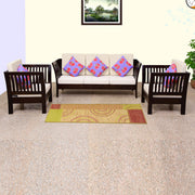 A walnut finish solid wood 5 seater sofa set consisting of three single sofas and two armchairs, with beige cushions and multicolored throw pillows, placed in a room with a carpet.