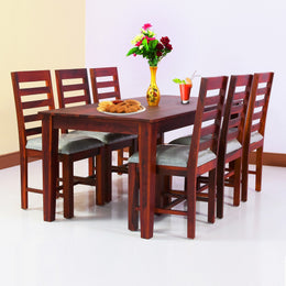 A wooden dining table with six chairs arranged around it in a dining room setting. The table is rectangular, and the chairs have a fabric seat cushion.