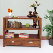A solid wood bookshelf with drawers in a brown finish, with books, a plant, and decorative items on it.