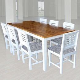 A wooden dining table with a white finish accompanied by eight chairs with white frames and brown leather seats, set against a room with large windows.