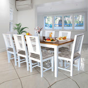 A white finish mango wood dining table set for 8 with rectangular tabletop and chairs featuring slatted back designs and leather upholstery, set in a kitchen environment.