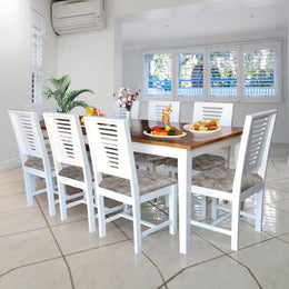 A white finish mango wood dining table set for 8 with rectangular tabletop and chairs featuring slatted back designs and leather upholstery, set in a kitchen environment.