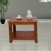 A rectangular solid wood coffee and tea table with a plant and a tea set on it, placed on a plain floor.