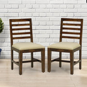 Two wooden dining chairs with a walnut finish, featuring a solid backrest and a cushioned seat, positioned in front of a white brick wall.