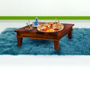 A rectangular teak wood chowki with pooja items setup on it, placed on a blue fuzzy surface.