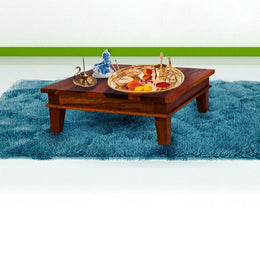 A rectangular teak wood chowki with pooja items setup on it, placed on a blue fuzzy surface.