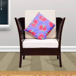 A wooden single seater sofa with a white cushion and a floral cushion on top, placed in a room with a light background.