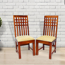 A pair of solid wood high back dining chairs with beige upholstered seats, positioned against a white brick wall.