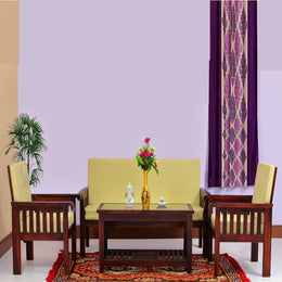 A solid wood sofa set with a coffee table arranged on a rug in a room with a purple wall and a window with a purple curtain.
