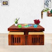 A solid wood honey finish coffee table with four stools underneath, placed in a room with decorative items.