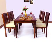 A solid wood dining table with a maple finish, accompanied by six chairs with beige upholstery. The table is set with a floral centerpiece and some decorative items.