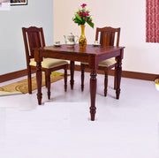 A wooden dining table with two chairs, featuring a maple finish, set in a room with a floral arrangement and tea set on the table.