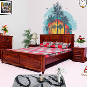 A wooden queen size double bed with a honey finish, featuring a headboard, footboard, and laid out with bedding. The room it's in has a colorful wall painting, a nightstand, and a dresser with a mirror.