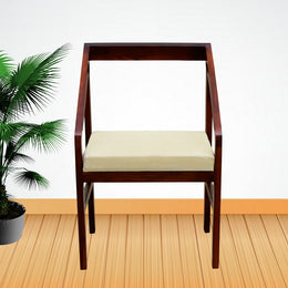 A wooden armchair with a cushion, made of sheesham wood with teak accents, placed on a wooden floor next to a potted plant.