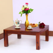 A rectangular solid wood center coffee table in maple finish, with a vase of flowers and a tea set on top, placed against a white background.