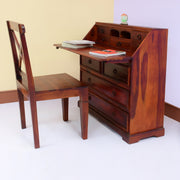A wooden chest of drawers with a pull-out study table and a matching chair, finished in maple, displayed in a living room setting.