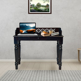 Black desk with a laptop, books, and a plant in a room with a gray wall and a small table.